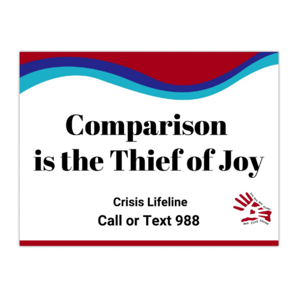 Sign says, "Comparison is the Thief of Joy" with the crisis lifeline that says, "Call or text 988" with the suicide prevention awareness colors and the Our City Cares Logo at the bottom.
